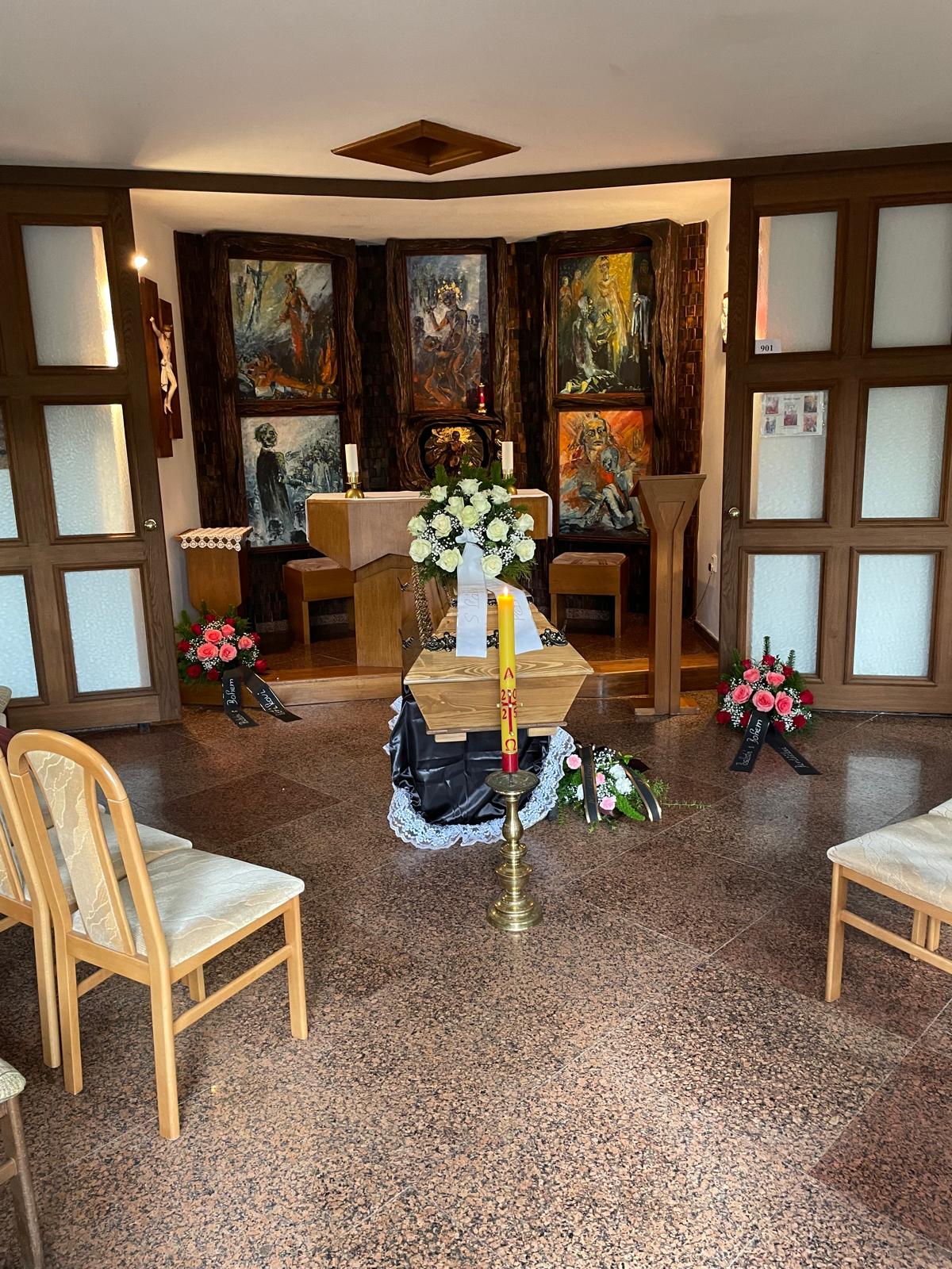 Poslední rozloučení ve smuteční síni s květinovou výzdobou a paškálem