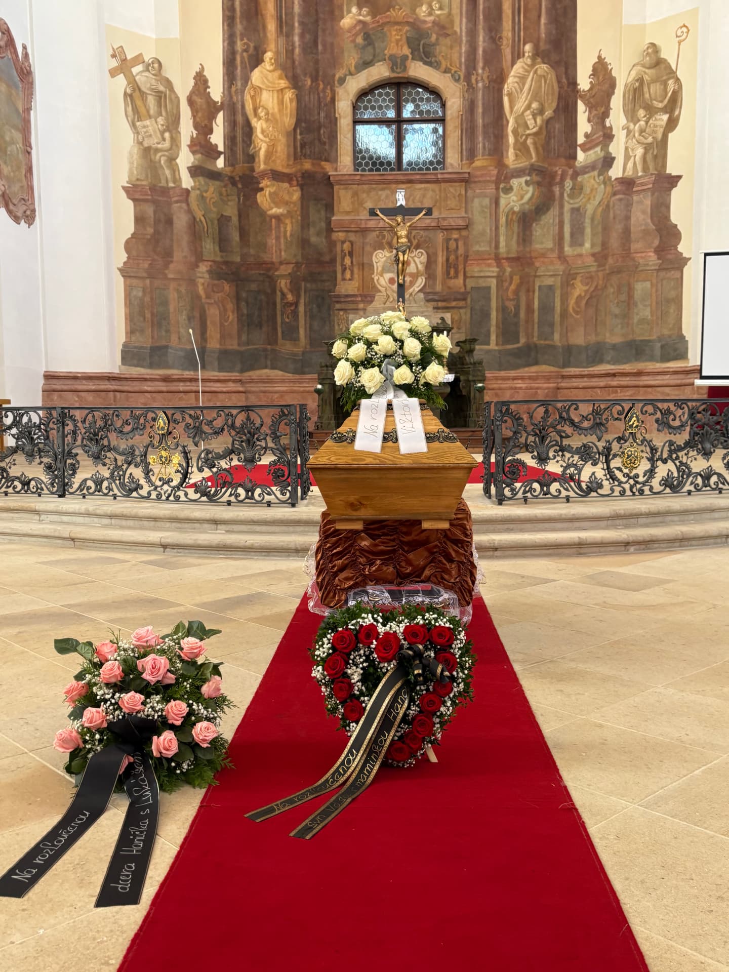 Poslední rozloučení v kostele s bílou kyticí na rakvi a smutečními věnci